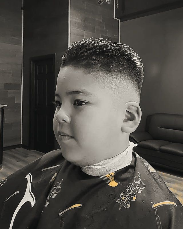 A boy with a short crop and faded sides, seated in the barber chair.