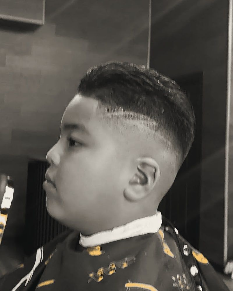 A boy in profile with a fade and a shaved part line.