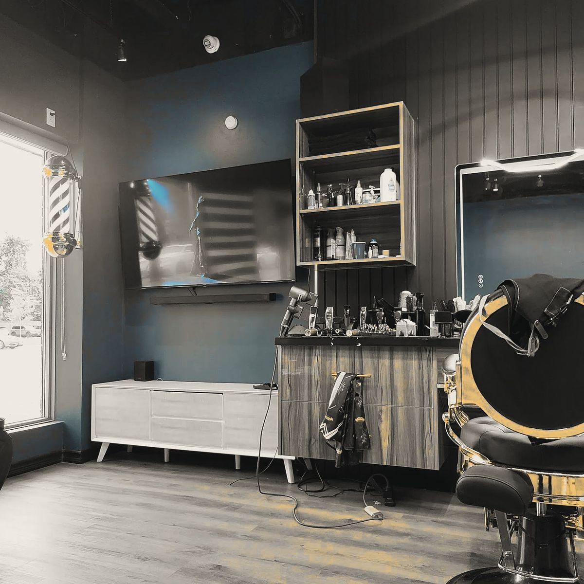 A barber station at KS Ghost: wood shelving, a wall-mounted screen and a gold-and-black barber chair.