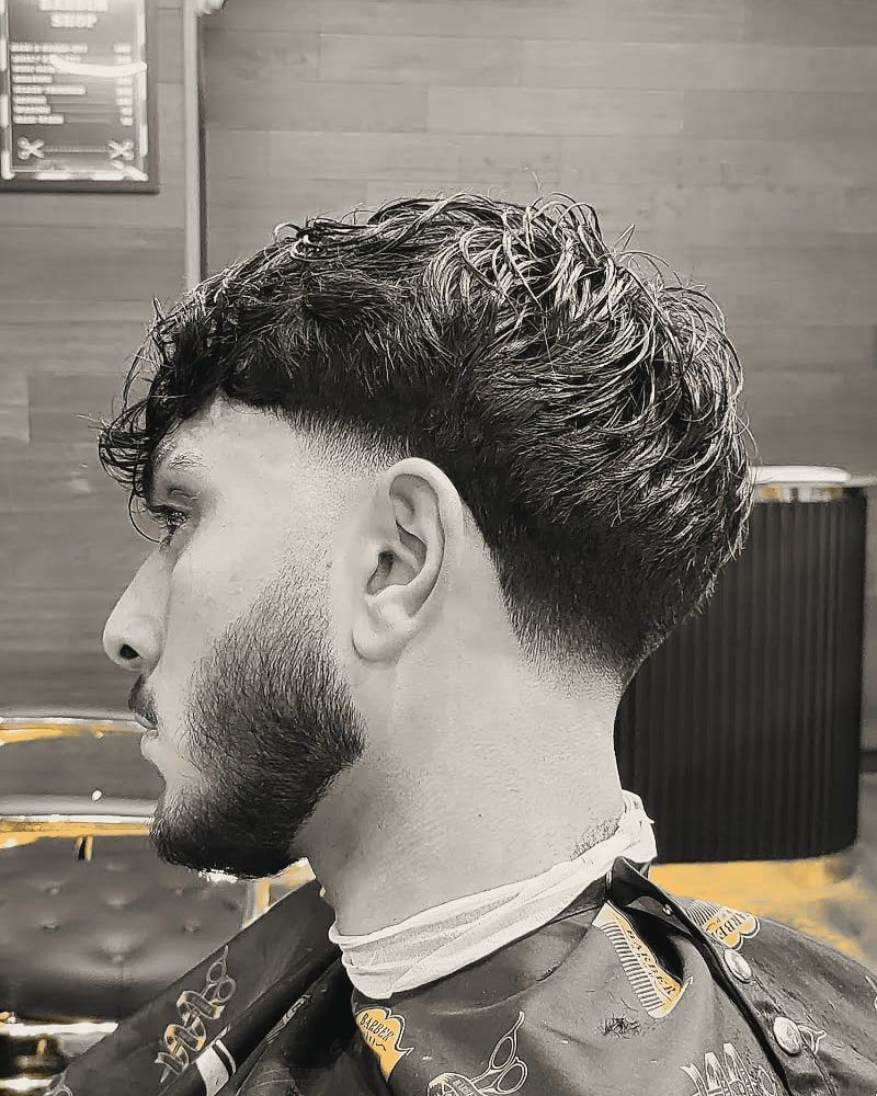 A loose curly fringe over a low fade, with a shaped beard.