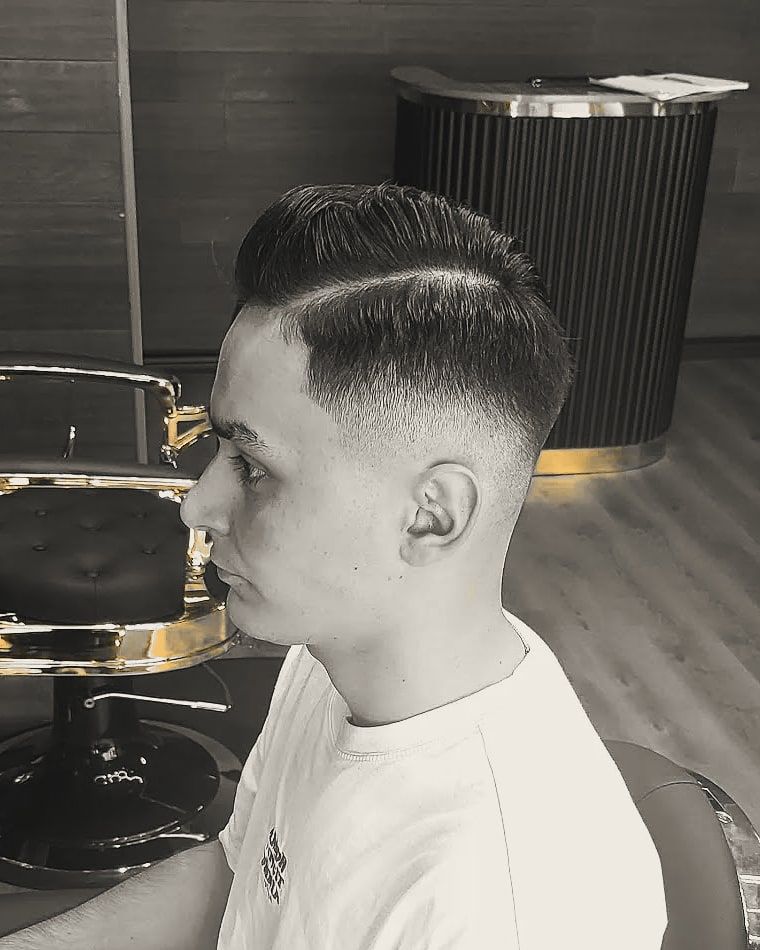 A young man with a combed side part and a skin fade.