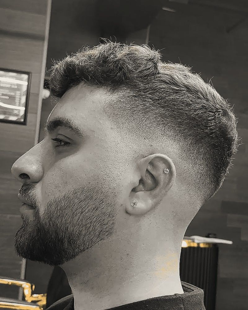 Side view of a skin fade with a short textured top and a trimmed beard.